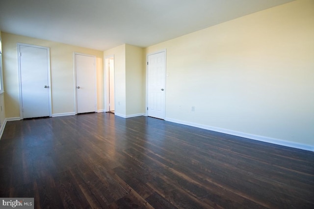 unfurnished bedroom featuring dark wood-style floors, baseboards, and two closets