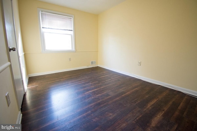 unfurnished room featuring dark wood-style floors, visible vents, and baseboards