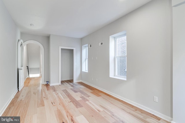 spare room featuring arched walkways, baseboards, visible vents, and light wood-style floors