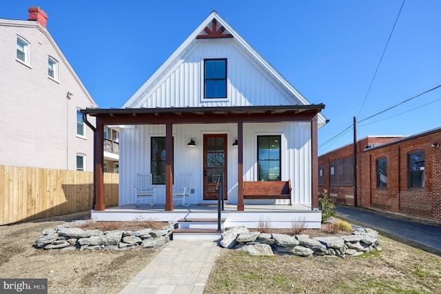 modern farmhouse with covered porch, board and batten siding, and fence