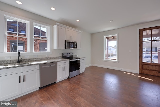 kitchen with appliances with stainless steel finishes, a sink, dark wood finished floors, and baseboards