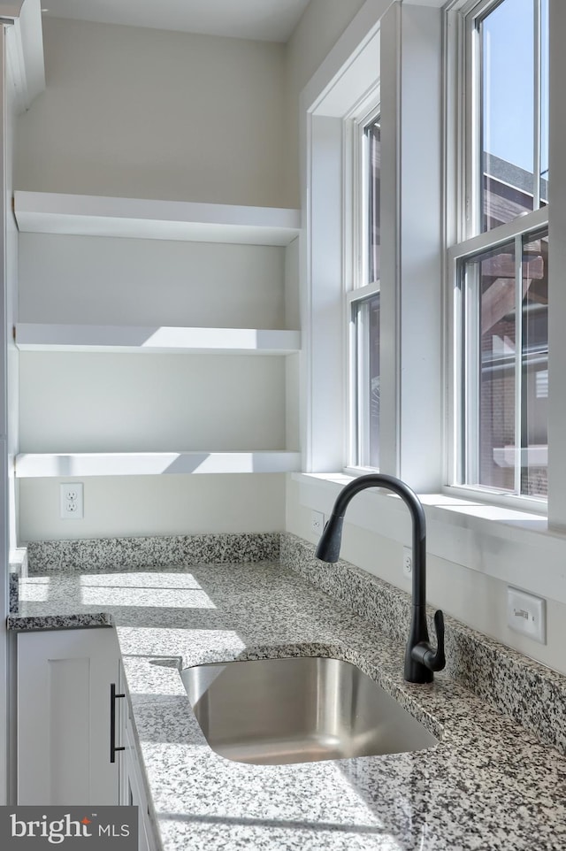 interior details with white cabinets, light stone countertops, open shelves, and a sink