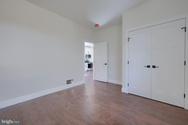 unfurnished bedroom featuring visible vents, a closet, baseboards, and wood finished floors