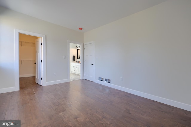 unfurnished bedroom featuring a closet, a spacious closet, baseboards, and wood finished floors