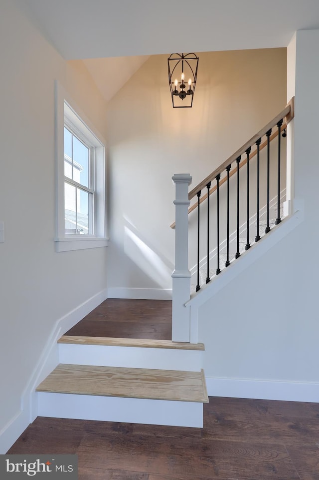 stairs featuring lofted ceiling, an inviting chandelier, baseboards, and wood finished floors