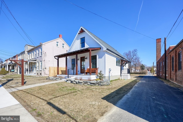 bungalow-style home with board and batten siding, a residential view, covered porch, and roof with shingles