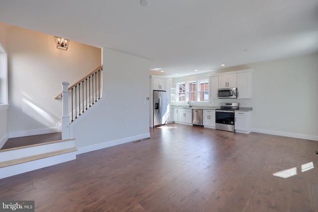 unfurnished living room with a sink, stairs, baseboards, and dark wood-style flooring