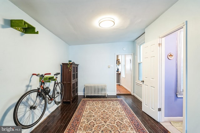 hall featuring wood-type flooring, baseboards, and radiator heating unit