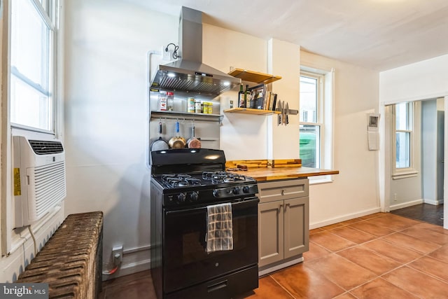 kitchen featuring light tile patterned floors, island range hood, butcher block counters, black gas stove, and baseboards