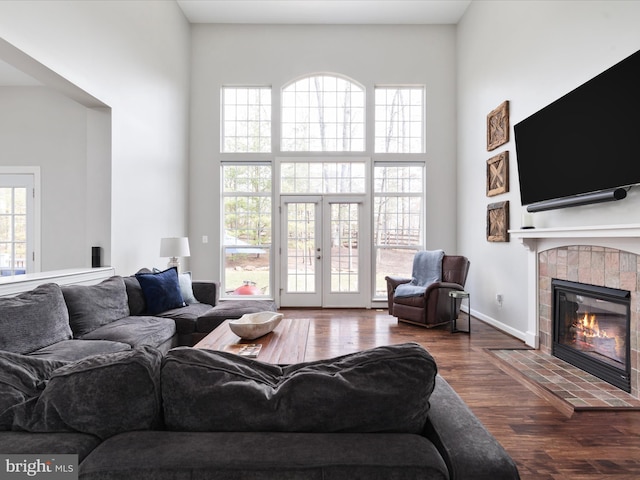 living area featuring a tile fireplace, a healthy amount of sunlight, a towering ceiling, and wood finished floors