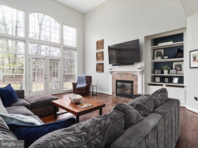 living room with built in features, a tile fireplace, dark wood-type flooring, a high ceiling, and french doors