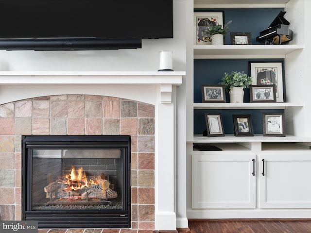 interior details featuring built in features, a tiled fireplace, and wood finished floors