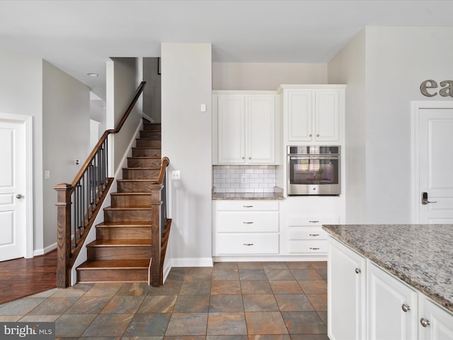 kitchen with light stone counters, white cabinetry, oven, and decorative backsplash