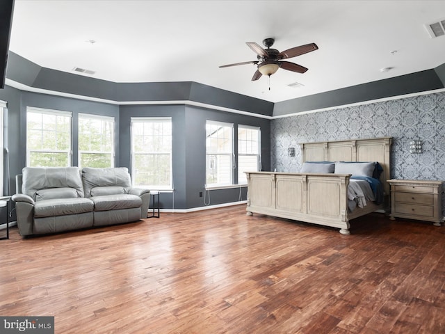 bedroom featuring baseboards, wood finished floors, visible vents, and wallpapered walls