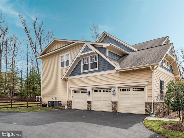 view of home's exterior with aphalt driveway, stone siding, roof with shingles, and fence