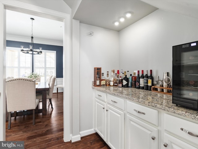 bar with a chandelier, lofted ceiling, dark wood-style flooring, wainscoting, and a bar