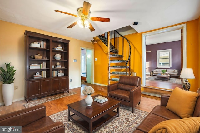 living room with baseboards, stairs, a ceiling fan, and wood finished floors