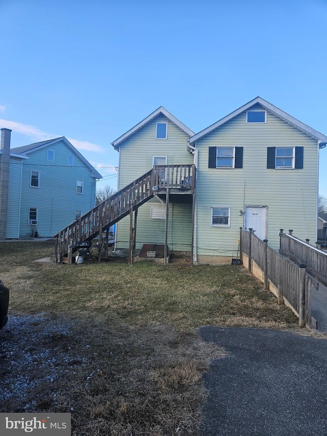 rear view of house with stairs, fence, a deck, and a lawn