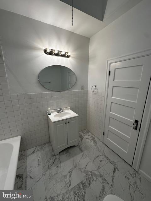 full bath featuring vanity, tile walls, marble finish floor, wainscoting, and a bathtub