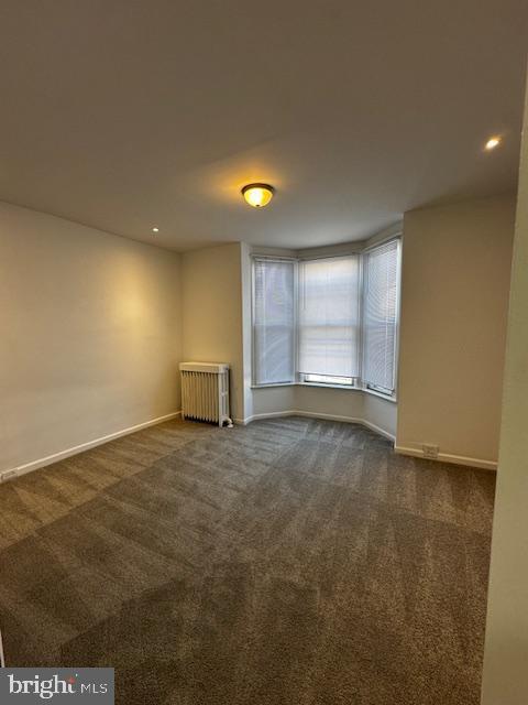 empty room featuring carpet, radiator heating unit, and baseboards