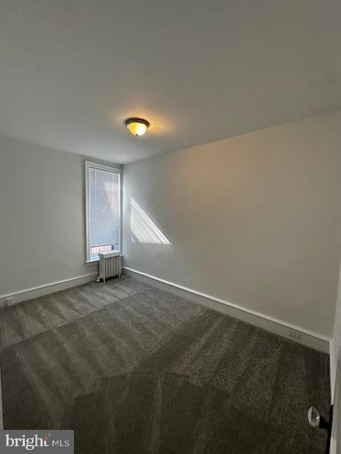 spare room with dark colored carpet, radiator heating unit, and baseboards