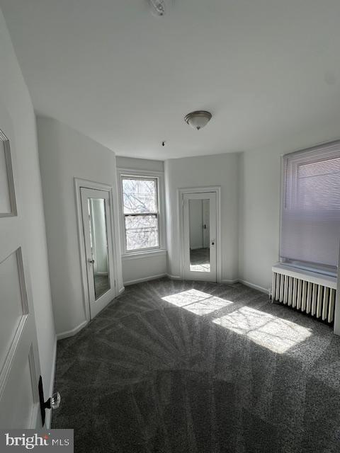 carpeted spare room featuring radiator and baseboards