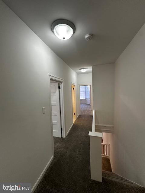 hallway featuring baseboards and dark colored carpet