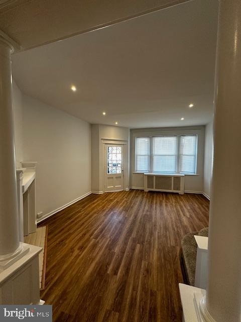 unfurnished living room with decorative columns, radiator heating unit, dark wood-style flooring, and recessed lighting