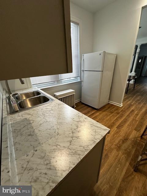 kitchen featuring dark wood-style floors, radiator, freestanding refrigerator, a sink, and baseboards