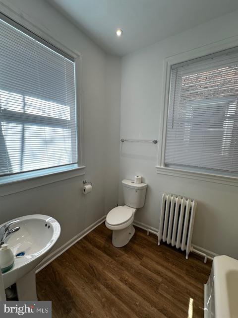 bathroom with baseboards, radiator, toilet, wood finished floors, and a bathtub