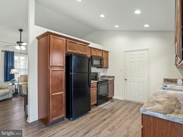 kitchen featuring light wood finished floors, brown cabinetry, vaulted ceiling, black appliances, and a sink