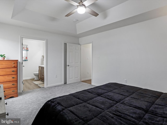 carpeted bedroom featuring ensuite bath, baseboards, a tray ceiling, and a ceiling fan