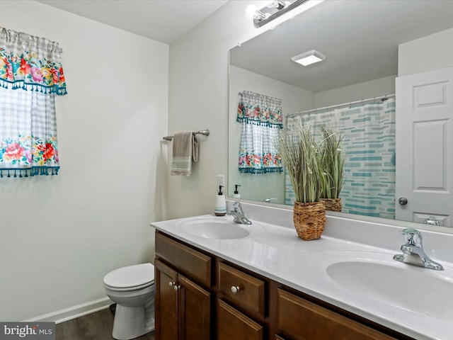 full bath featuring double vanity, a sink, toilet, and baseboards