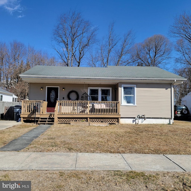 view of front of house featuring a shingled roof, a front yard, a wooden deck, and fence