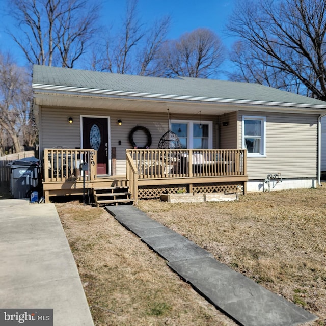 view of front of house with roof with shingles, a deck, and a front yard