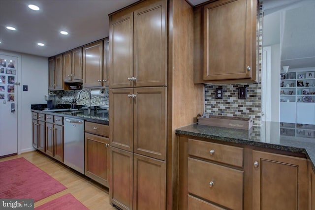 kitchen with light wood finished floors, dark stone countertops, dishwasher, and a sink