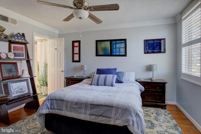 bedroom featuring light wood finished floors, visible vents, a textured ceiling, and crown molding