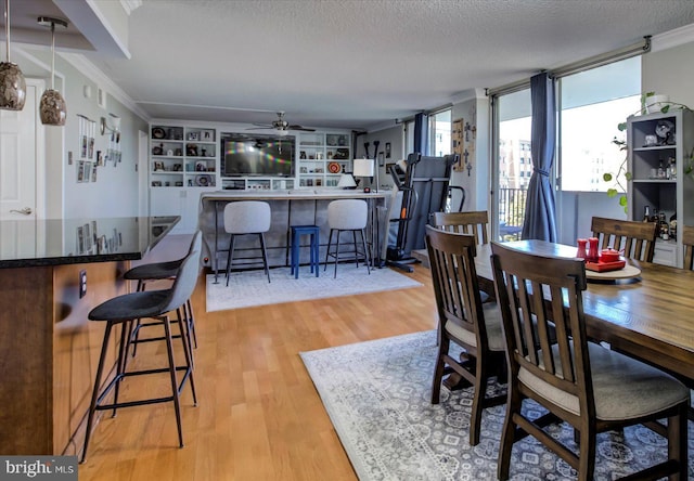 dining room with light wood-style flooring, ceiling fan, a textured ceiling, crown molding, and a dry bar