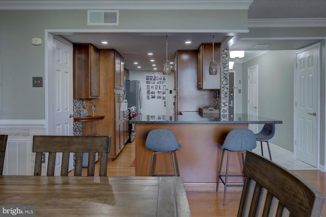 kitchen featuring visible vents, light wood-style flooring, ornamental molding, a kitchen breakfast bar, and backsplash