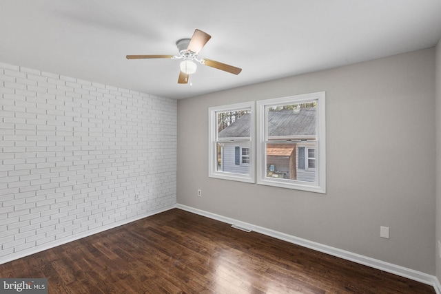 unfurnished room featuring dark wood-style floors, visible vents, baseboards, brick wall, and ceiling fan