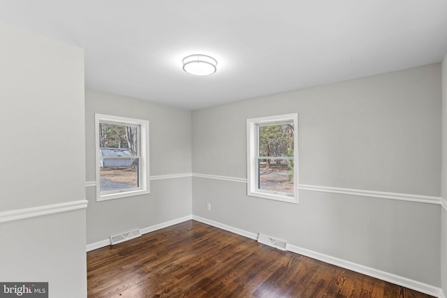 unfurnished room featuring visible vents, baseboards, and dark wood finished floors