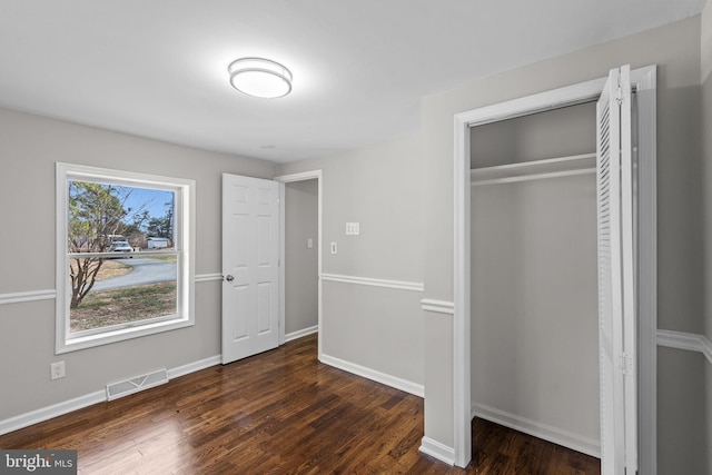 unfurnished bedroom featuring visible vents, baseboards, a closet, and wood finished floors