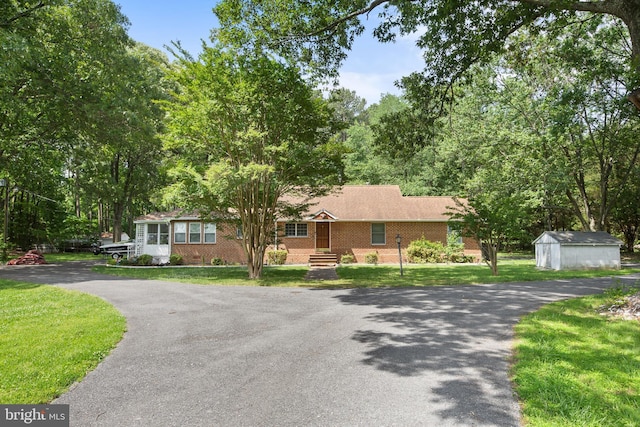 ranch-style home with driveway, brick siding, an outbuilding, and a front lawn