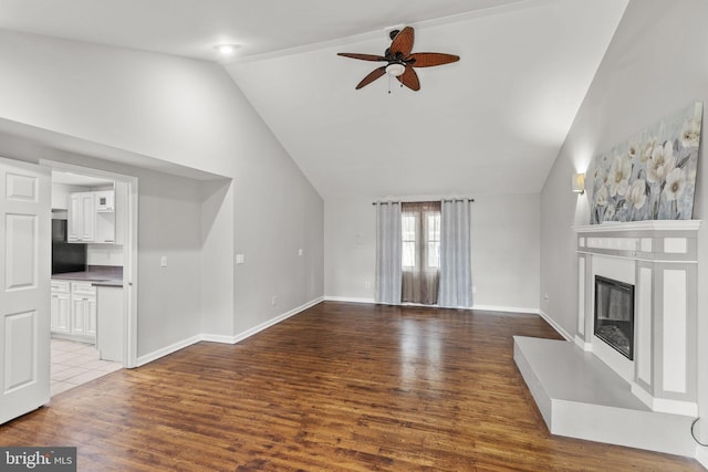 unfurnished living room with baseboards, ceiling fan, lofted ceiling, wood finished floors, and a glass covered fireplace