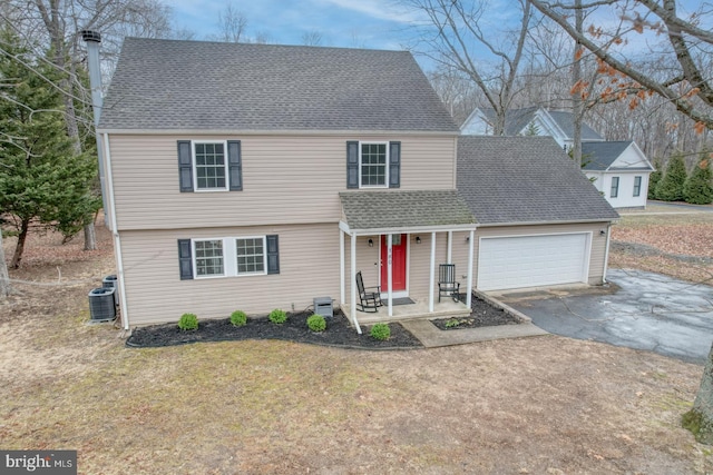 colonial-style house with aphalt driveway, cooling unit, roof with shingles, and an attached garage