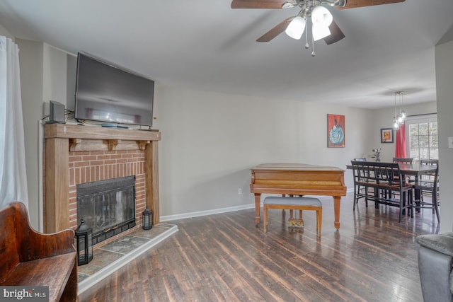 living area featuring ceiling fan with notable chandelier, a fireplace, baseboards, and wood finished floors