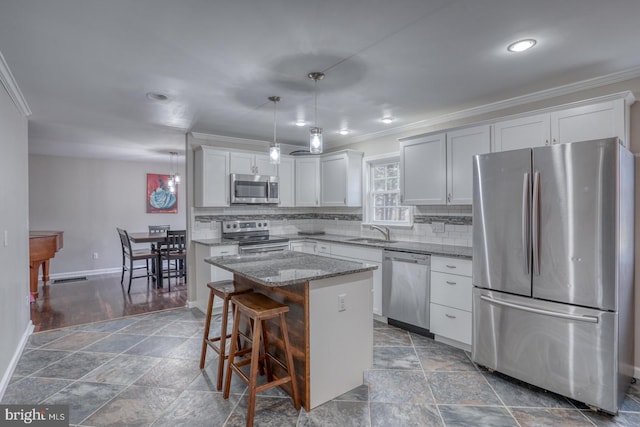 kitchen with light stone counters, backsplash, appliances with stainless steel finishes, a sink, and a kitchen island