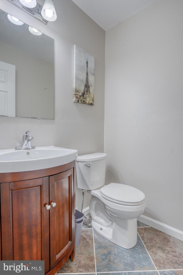 half bathroom featuring toilet, baseboards, and vanity