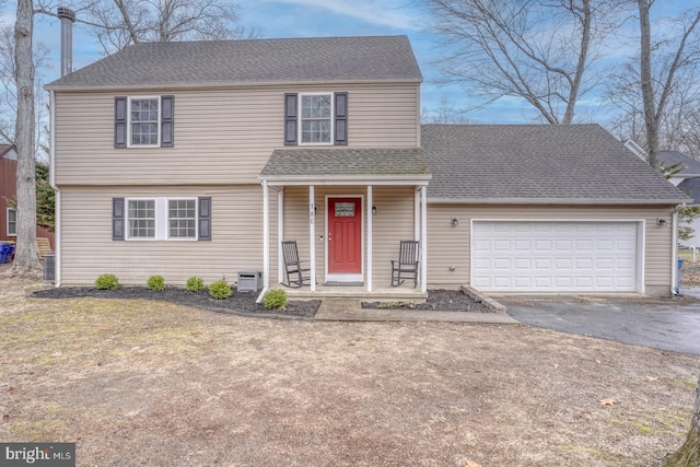 colonial house with covered porch, aphalt driveway, an attached garage, and a shingled roof