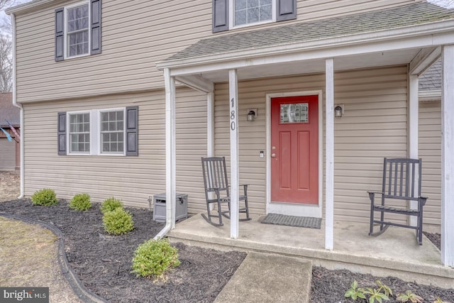 doorway to property with a porch and roof with shingles